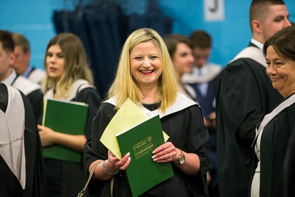 Graduate in ceremony holding graduation programme
