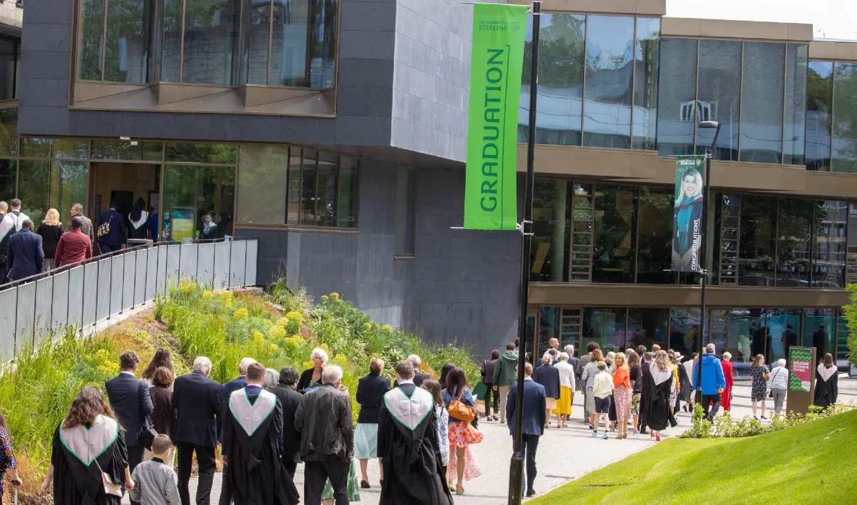 Graduates in robes walking by Campus Central