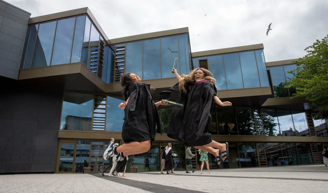 Two graduates jumping by Campus Central