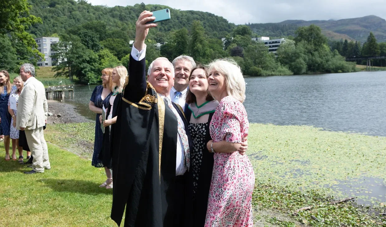 Chancellor poses with a family by loch after graduation