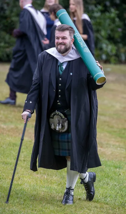 Male graduate poses with giant scroll prop