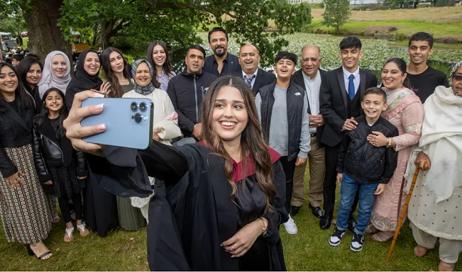 Graduate takes selfie with large family group behind