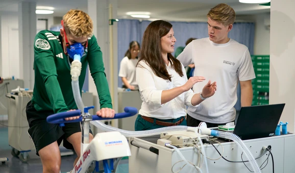 Sport researchers study student on exercise bike.