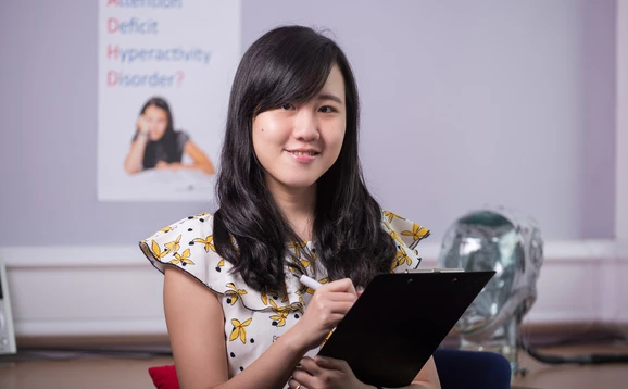 Postgraduate Taught psychology student holding clipboard with head simulator and psychology poster