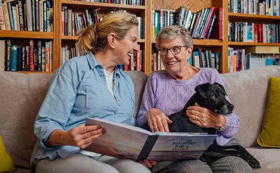 Two women sitting on a couch looking through a photo album