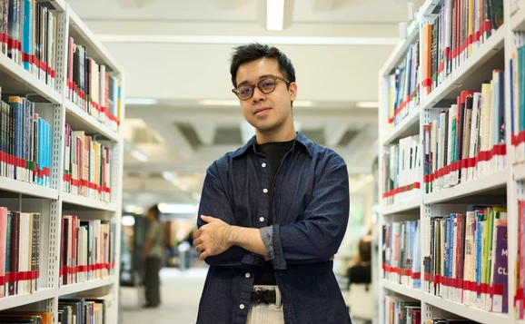 Postgraduate student standing between bookcases in the library