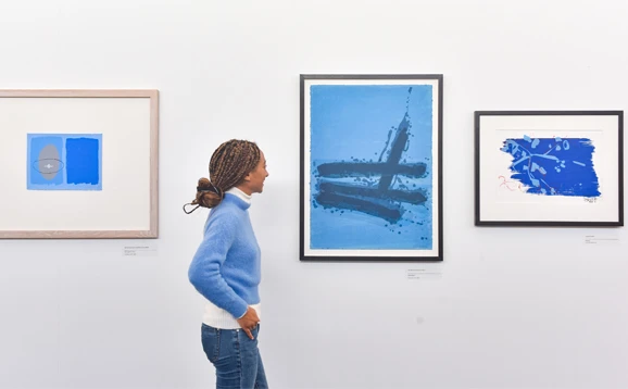 Three artworks hung on a wall. A woman is looking at one of the artworks.