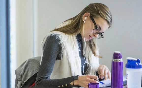 Student wearing glasses studying with earphones in