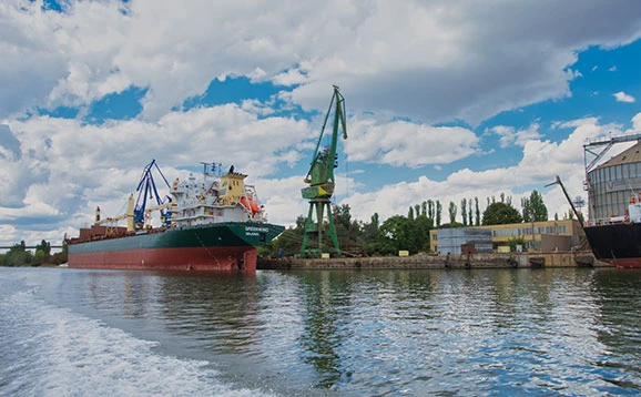 A ship tied up at a dock with a green crane next to it.