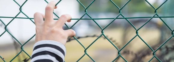 child's hands at fence