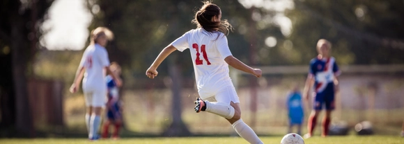 Girl wearing a white football strip shapes up to kick a football.
