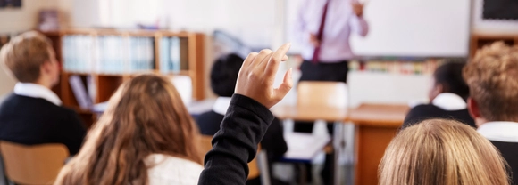 Stock photos of a classroom. A teacher stands in front of a whiteboard with students sitting at desks facing them.