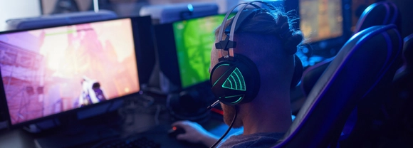 Rear view of young gamer wearing gaming headphones with backlight and playing in computer video game on computer