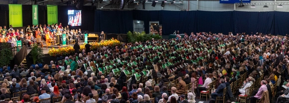 The graduation hall showing a seated crowd and members of University staff on stage during a ceremony.