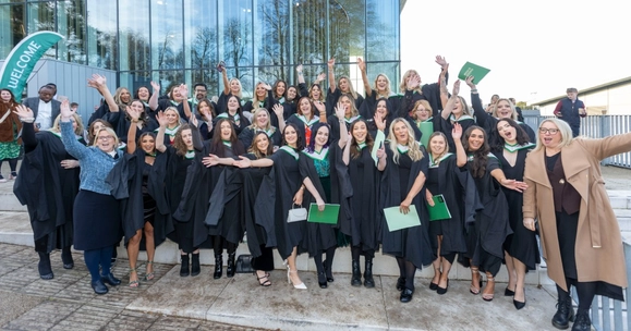 A large group of nursing students wearing graduation gowns pose on the steps outside the Sports Centre alongside NHS Forth Valley’s Executive Nurse Director Professor Frances Dodd and Director of Nursing Professor Karen Goudie