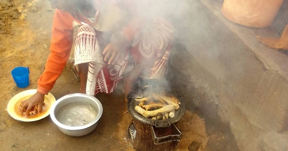 A woman sits over an open pan surrounded by smoke
