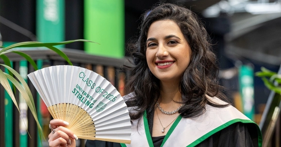 Graduate poses with University of Stirling branded fan.