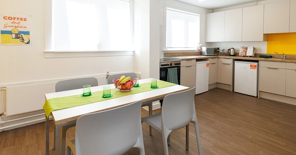 Kitchen in Muirhead House. Shows a table with chairs, and kitchen countertops with a yellow feature wall.