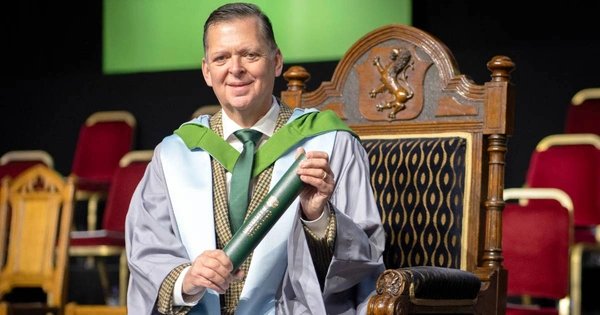 Stanley Morris sits on stage at the University of Stirling graduation ceremony. He wears graduation robes and holds a graduation scroll.