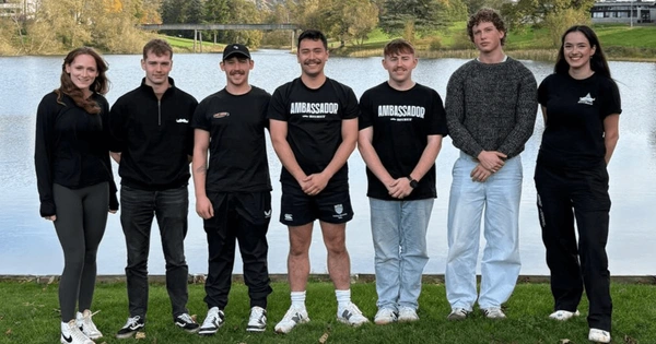 Seven Stirling students posing beside each other in front of the campus loch