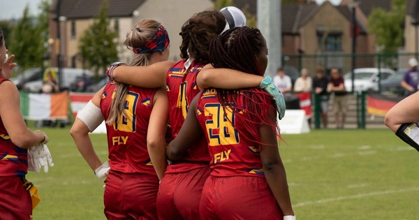 Three female flag football players stand arm-in-arm