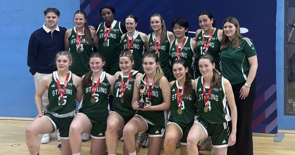 Women's basketball team pose with trophy.