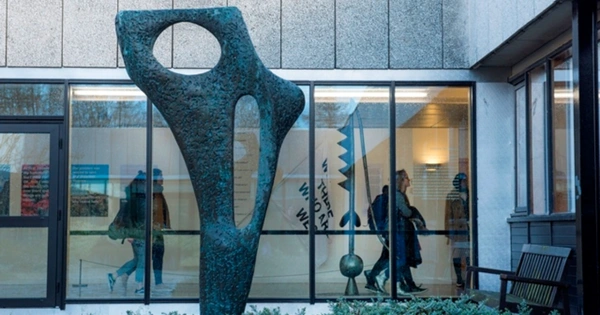 sculpture in front of windows with people walking by