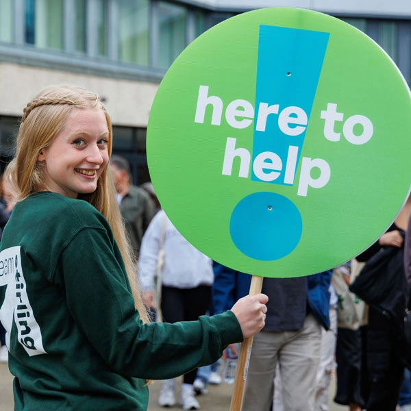 A helpful student with a lollipop sign which reads 'here to help'