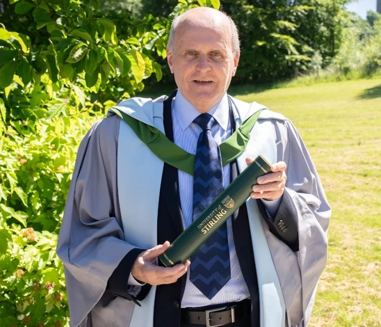 Dr Walter Humes poses with his graduation scroll on campus.