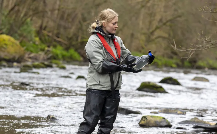 academic in river analysing a water sample
